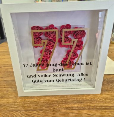Zahl 77 aus rosa Blumen, umgeben von einem Rahmen mit Geburtstagsgratulation.