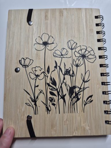 Holznotizbuch mit schwarzem Blumenmuster auf der Vorderseite.