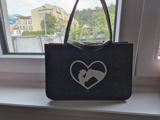 Schwarze Tasche mit Herzmotiv und einer dargestellten Umarmung.