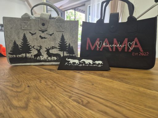 Drei Tragetaschen: eine mit Waldmotiven, eine mit "MAMA" Schriftzug und eine schwarze Tasche.