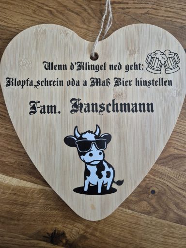 Holzschild in Herzform mit Kuhmotiv und Text in Dialekt über Familie Frantschmann.