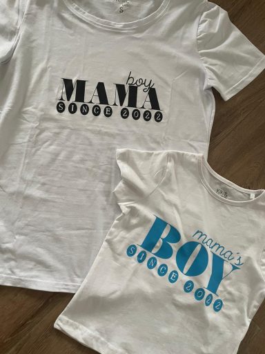 Weiße T-Shirts mit den Aufschriften "MAMA" und "mommy's BOY" in schwarzer und blauer Schrift.