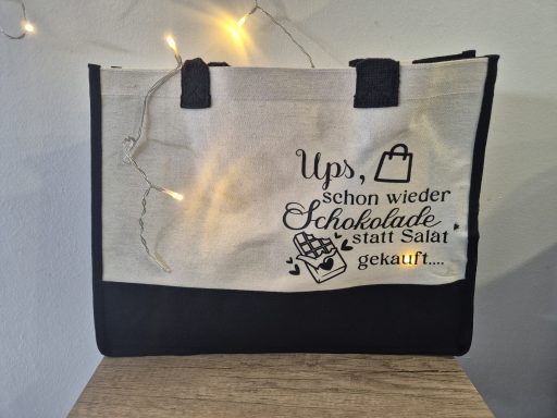 Beige Tasche mit schwarzem Boden und Spruch über Schokolade.